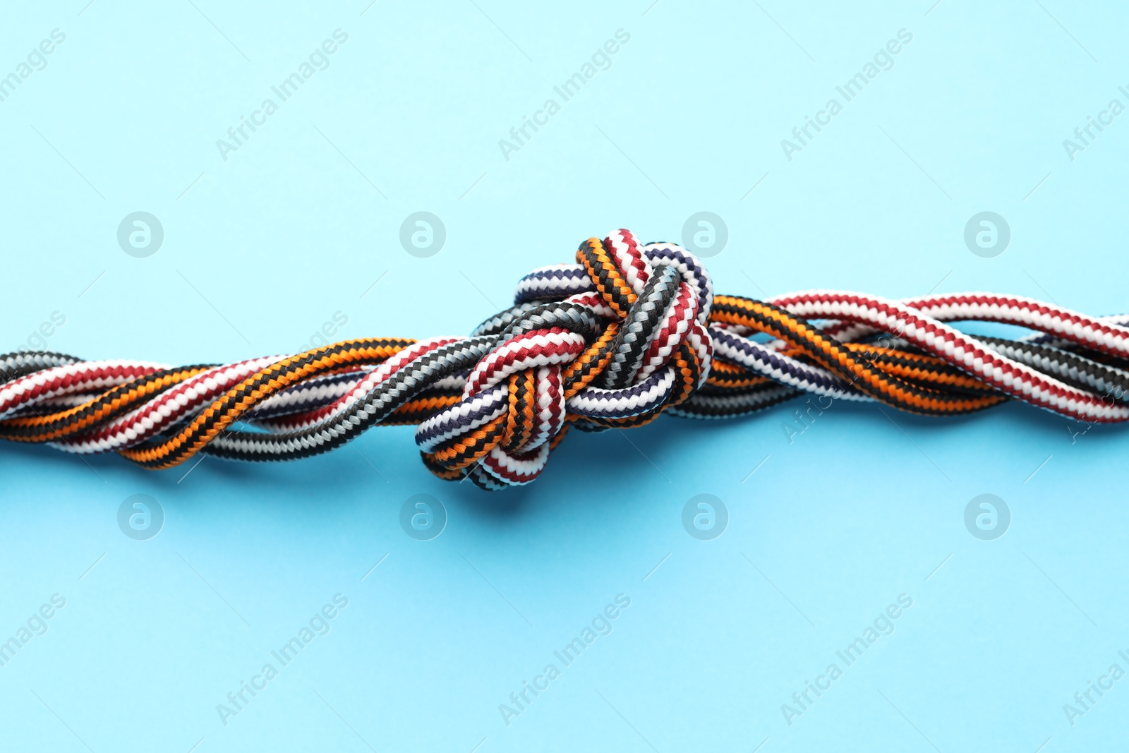 Photo of Colorful ropes tied in knot on light blue background, top view. Unity concept