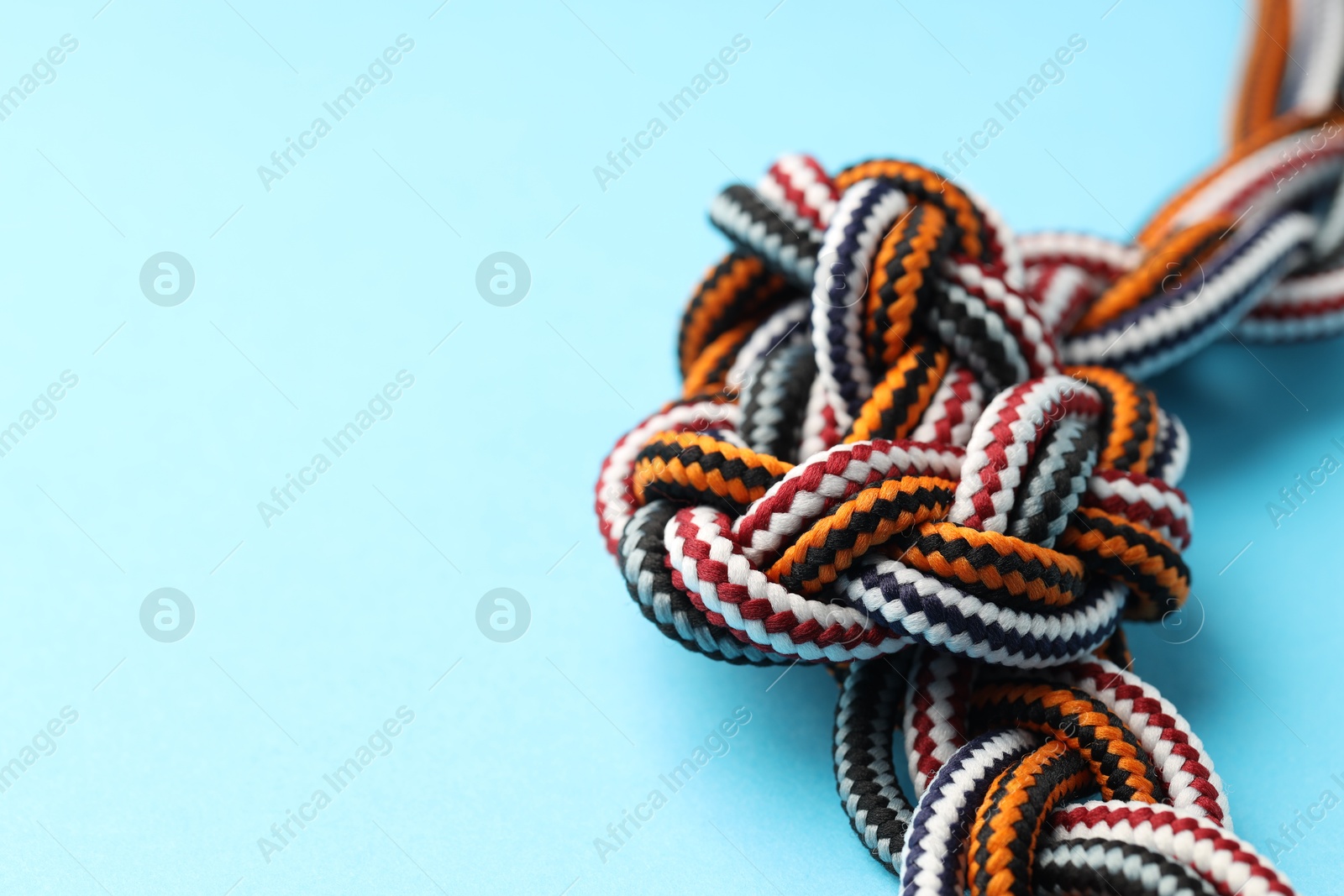 Photo of Colorful ropes tied in knot on light blue background, closeup and space for text. Unity concept