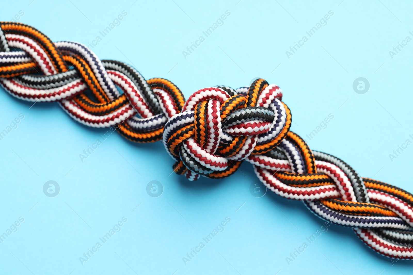 Photo of Colorful ropes tied in knot on light blue background, top view. Unity concept