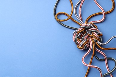 Photo of Colorful ropes tied in knot on blue background, top view and space for text. Unity concept