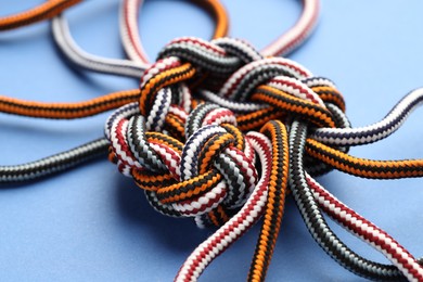 Colorful ropes tied in knot on blue background, closeup. Unity concept