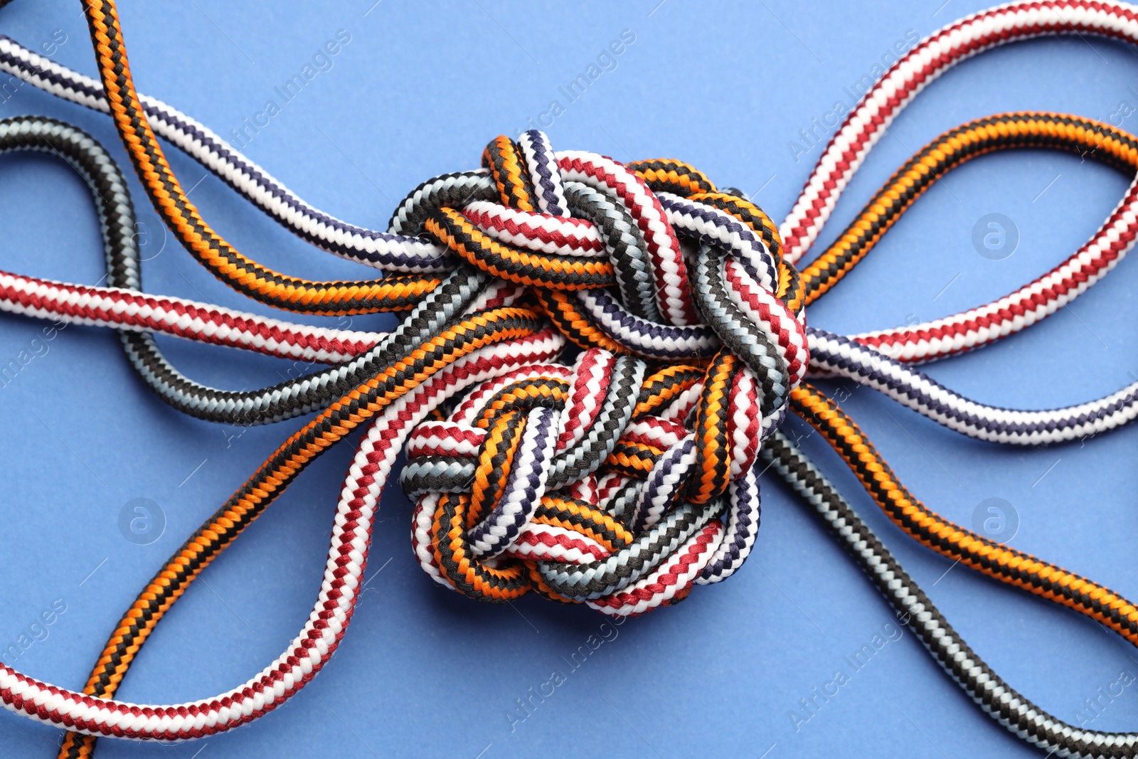 Photo of Colorful ropes tied in knot on blue background, top view. Unity concept