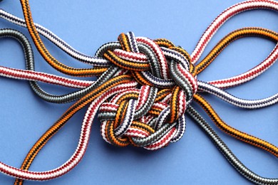 Photo of Colorful ropes tied in knot on blue background, top view. Unity concept