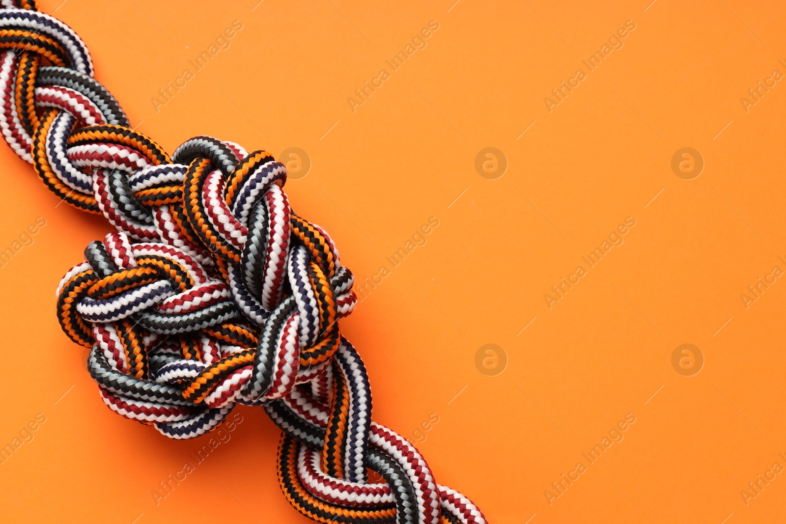 Photo of Colorful ropes tied in knot on orange background, top view and space for text. Unity concept