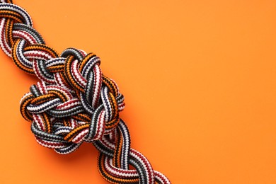 Photo of Colorful ropes tied in knot on orange background, top view and space for text. Unity concept