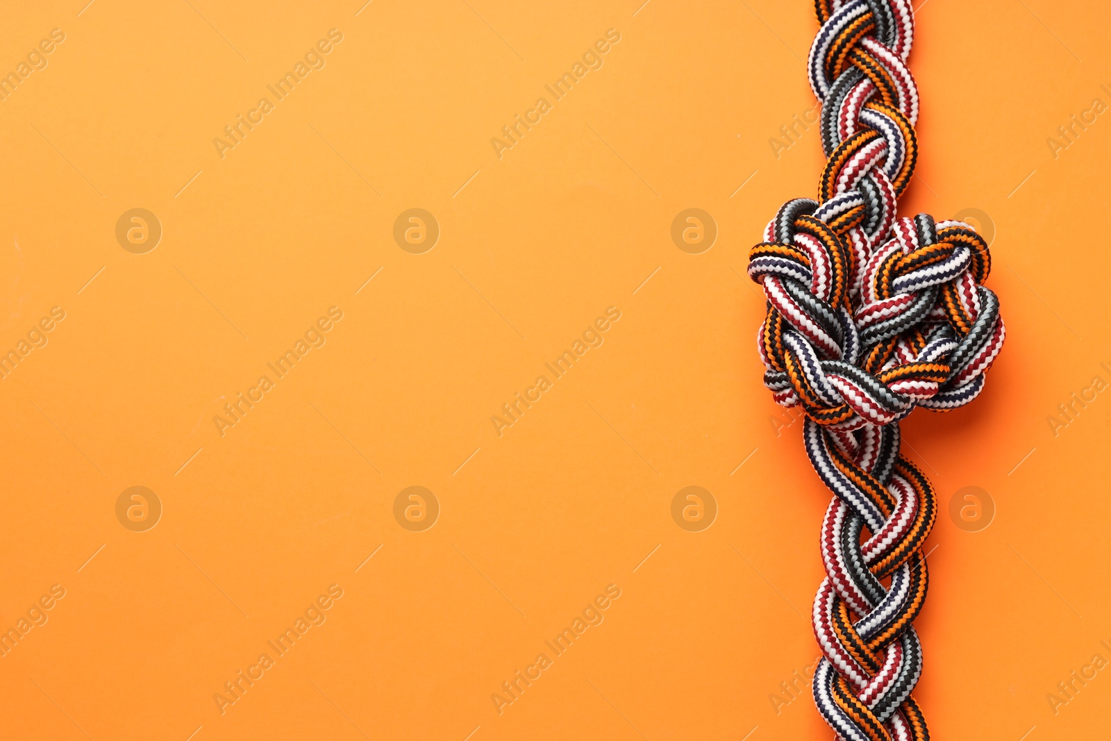 Photo of Colorful ropes tied in knot on orange background, top view and space for text. Unity concept