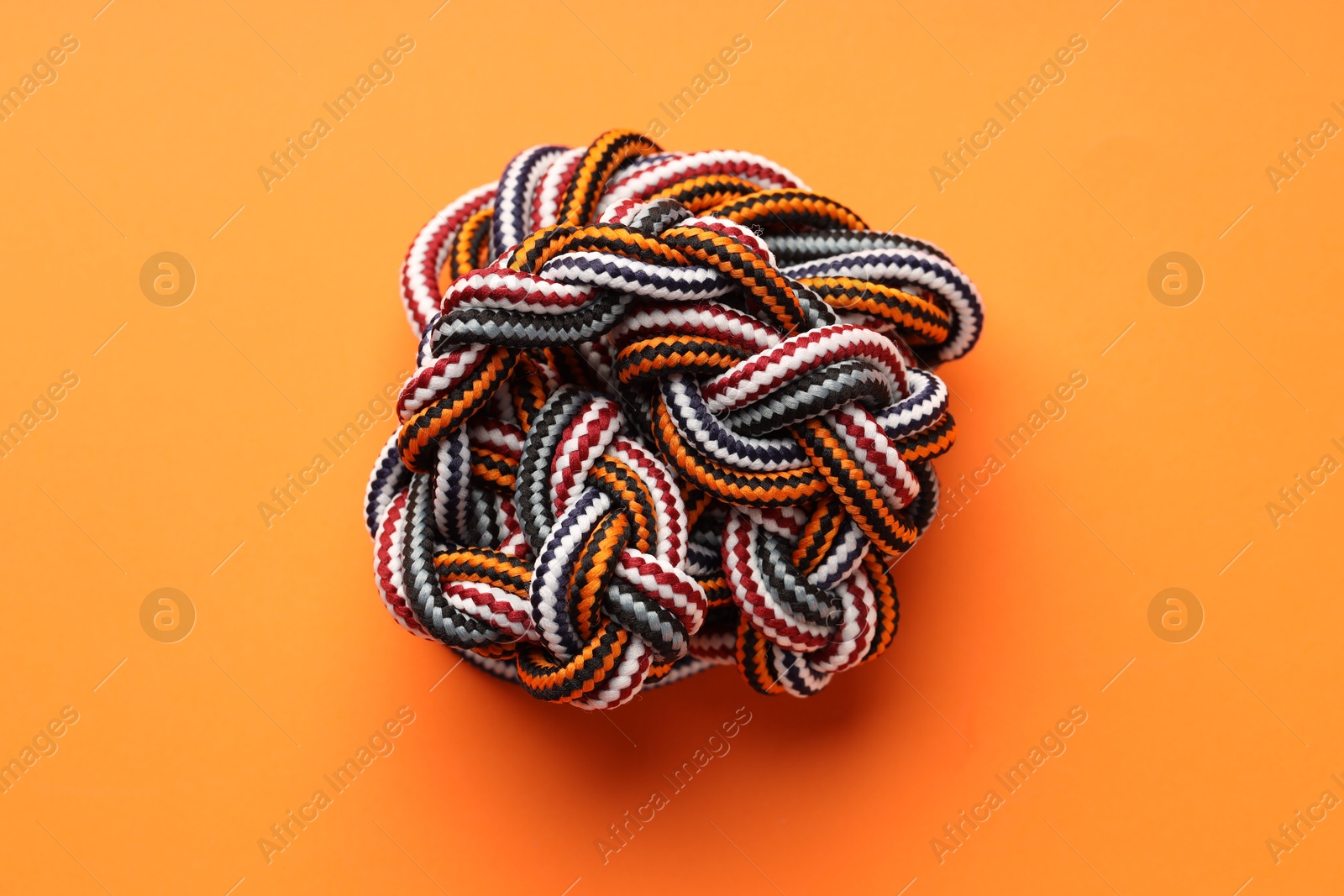 Photo of Colorful ropes tied in knot on orange background, top view. Unity concept