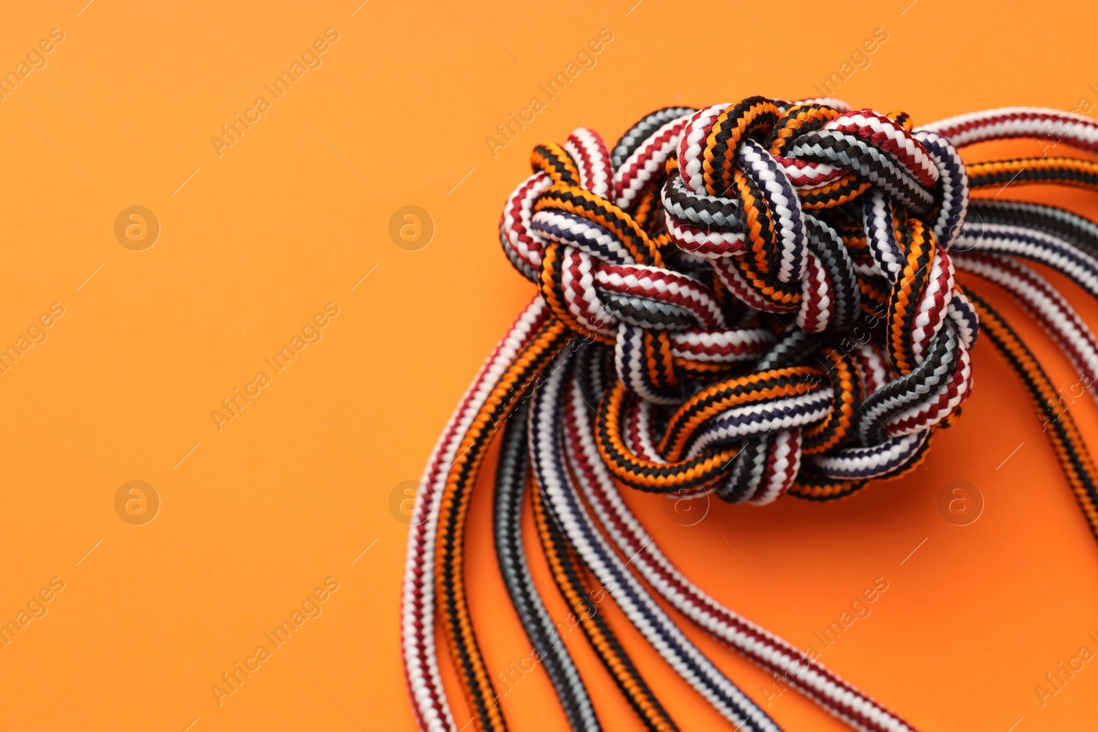 Photo of Colorful ropes tied in knot on orange background, top view and space for text. Unity concept