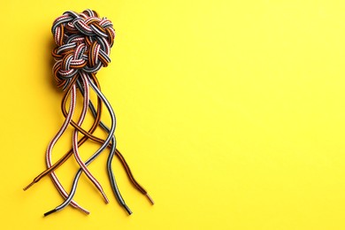 Photo of Colorful ropes tied in knot on yellow background, top view and space for text. Unity concept