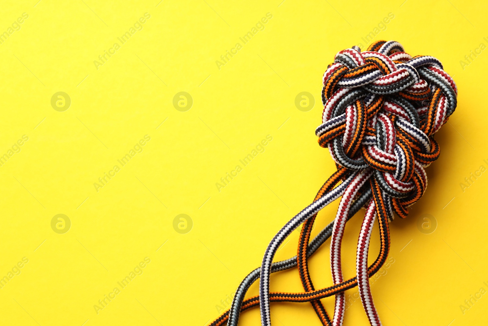 Photo of Colorful ropes tied in knot on yellow background, top view and space for text. Unity concept