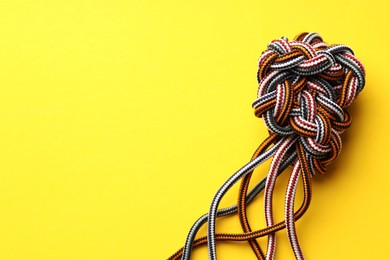 Photo of Colorful ropes tied in knot on yellow background, top view and space for text. Unity concept