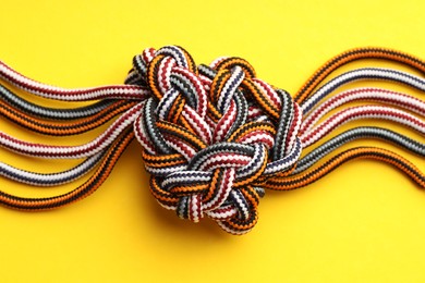 Colorful ropes tied in knot on yellow background, top view. Unity concept