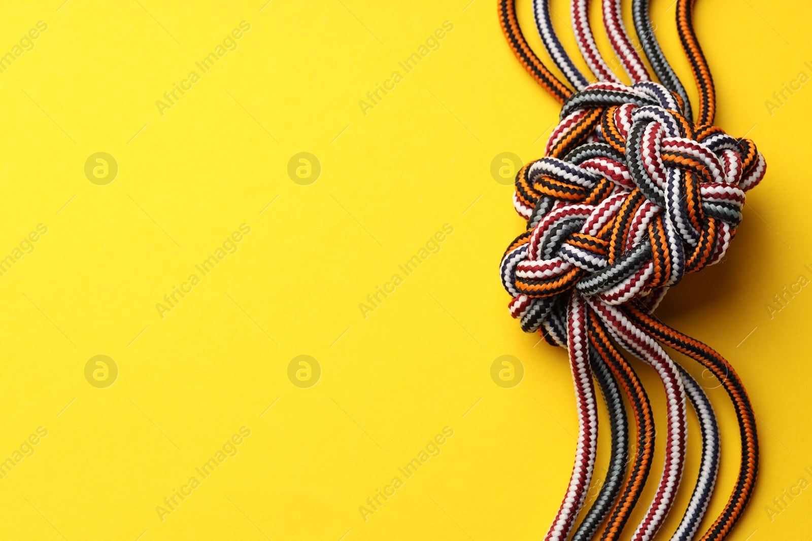 Photo of Colorful ropes tied in knot on yellow background, top view and space for text. Unity concept