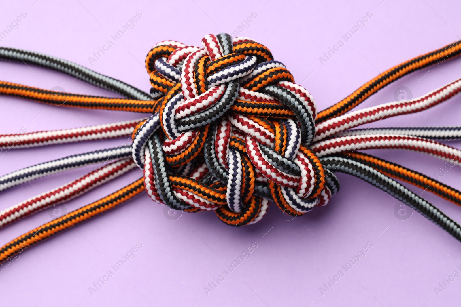 Photo of Colorful ropes tied in knot on violet background, top view. Unity concept