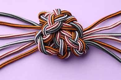 Colorful ropes tied in knot on violet background, top view. Unity concept