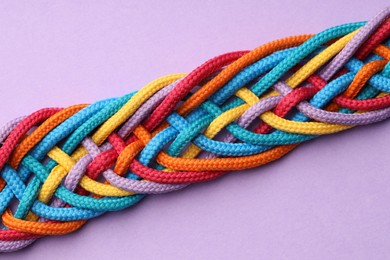 Photo of Colorful ropes tied together on violet background, top view. Unity concept