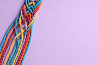 Photo of Colorful ropes tied together on violet background, top view and space for text. Unity concept