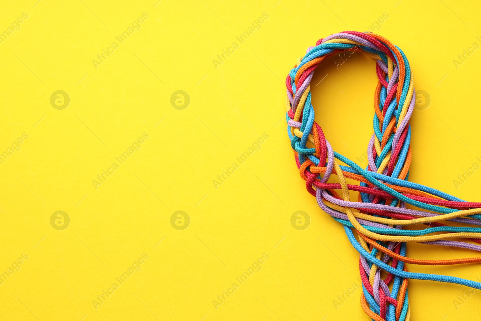 Photo of Colorful ropes tied together on yellow background, top view and space for text. Unity concept