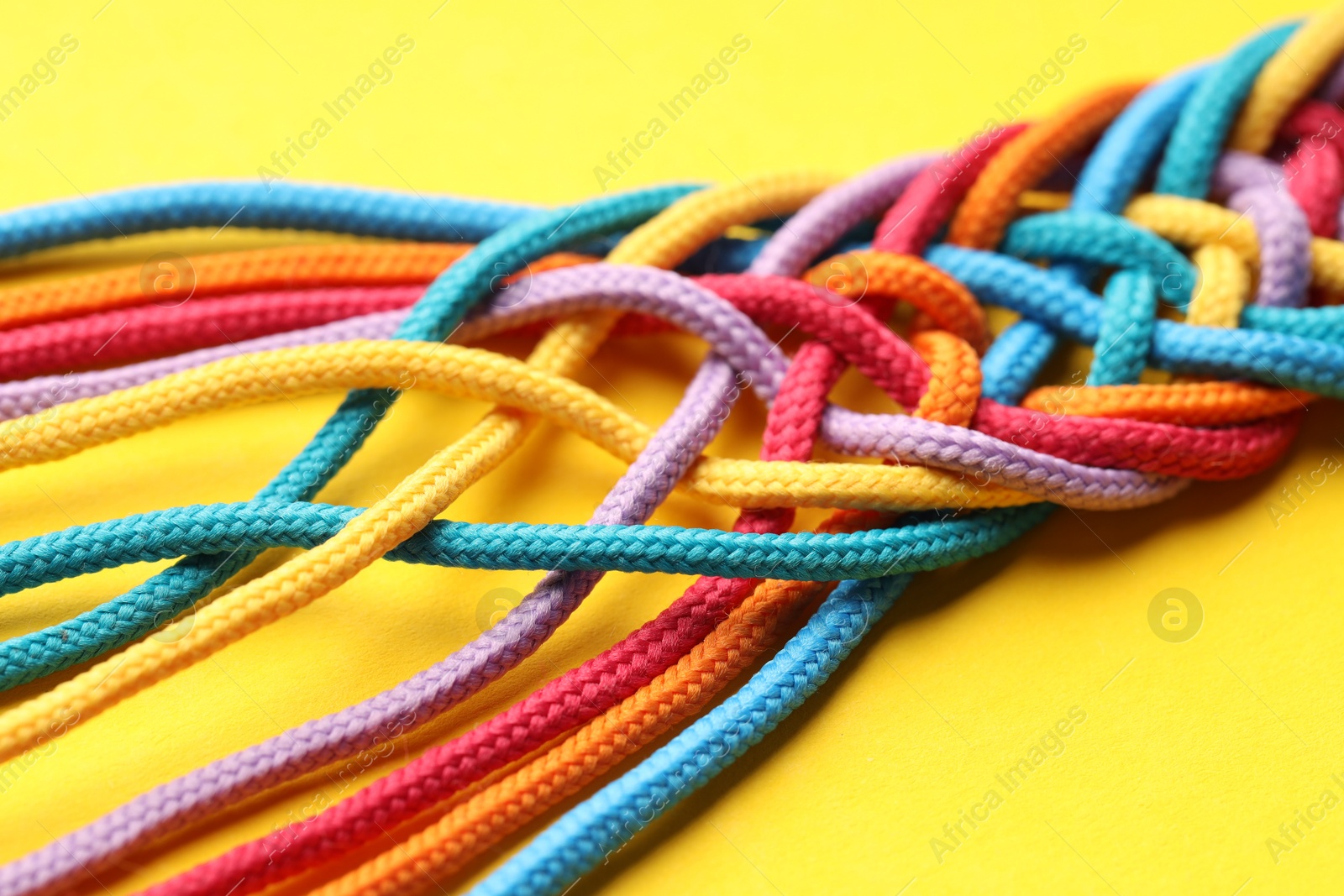 Photo of Colorful ropes tied together on yellow background, closeup. Unity concept