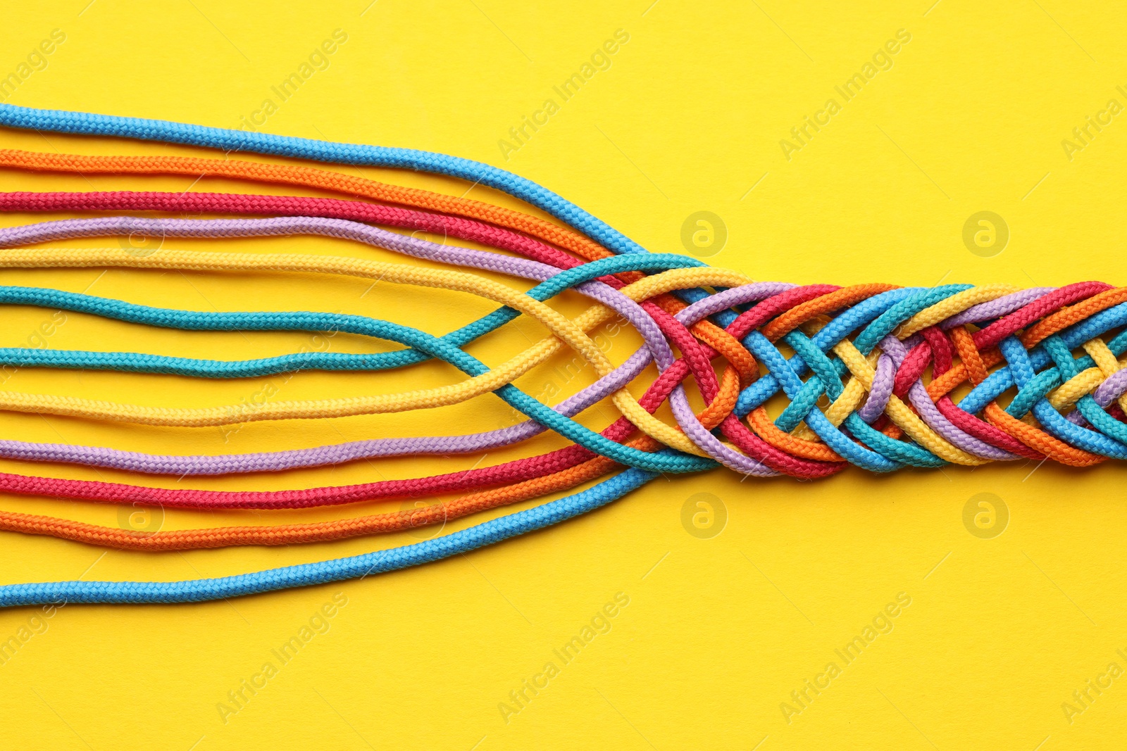 Photo of Colorful ropes tied together on yellow background, top view. Unity concept