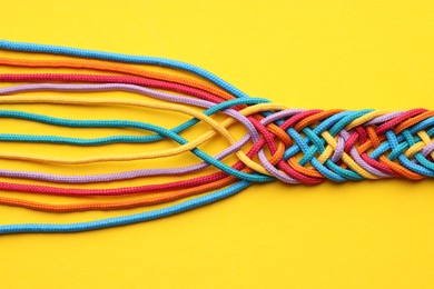 Photo of Colorful ropes tied together on yellow background, top view. Unity concept