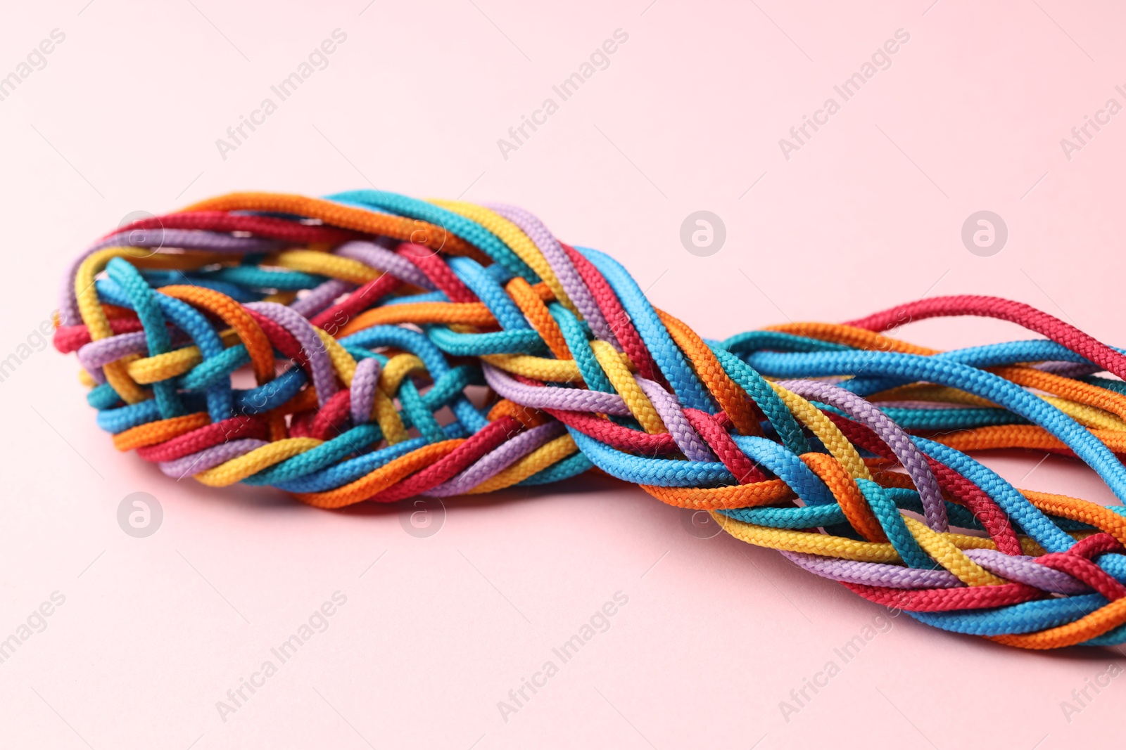 Photo of Colorful ropes tied together on pink background, closeup. Unity concept