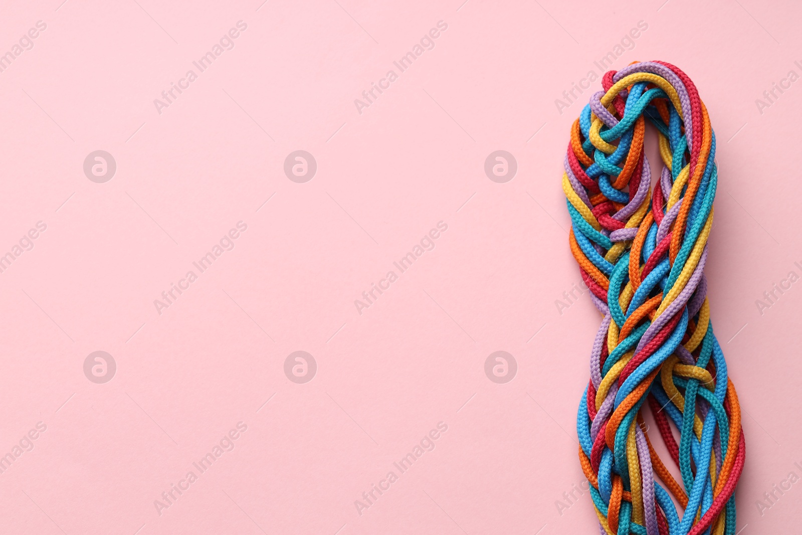 Photo of Colorful ropes tied together on pink background, top view and space for text. Unity concept