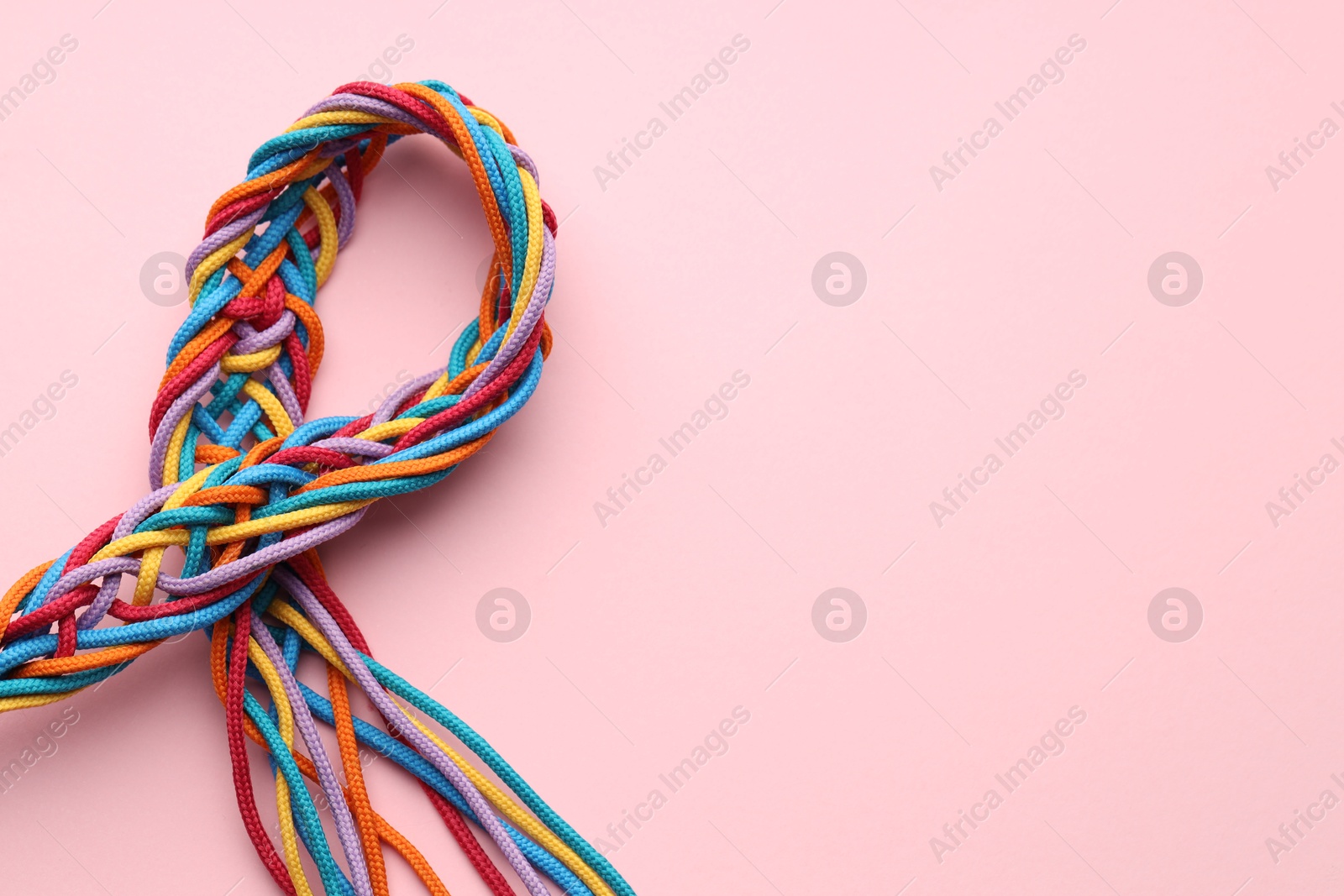 Photo of Colorful ropes tied together on pink background, top view and space for text. Unity concept