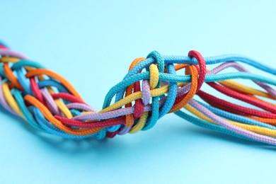 Photo of Colorful ropes tied together on light blue background, closeup. Unity concept