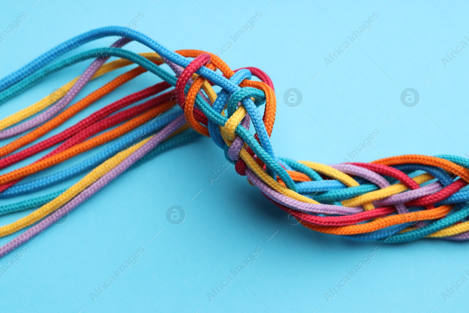 Photo of Colorful ropes tied together on light blue background, closeup. Unity concept