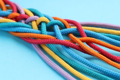 Photo of Colorful ropes tied together on light blue background, closeup. Unity concept