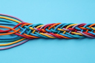 Photo of Colorful ropes tied together on light blue background, top view. Unity concept