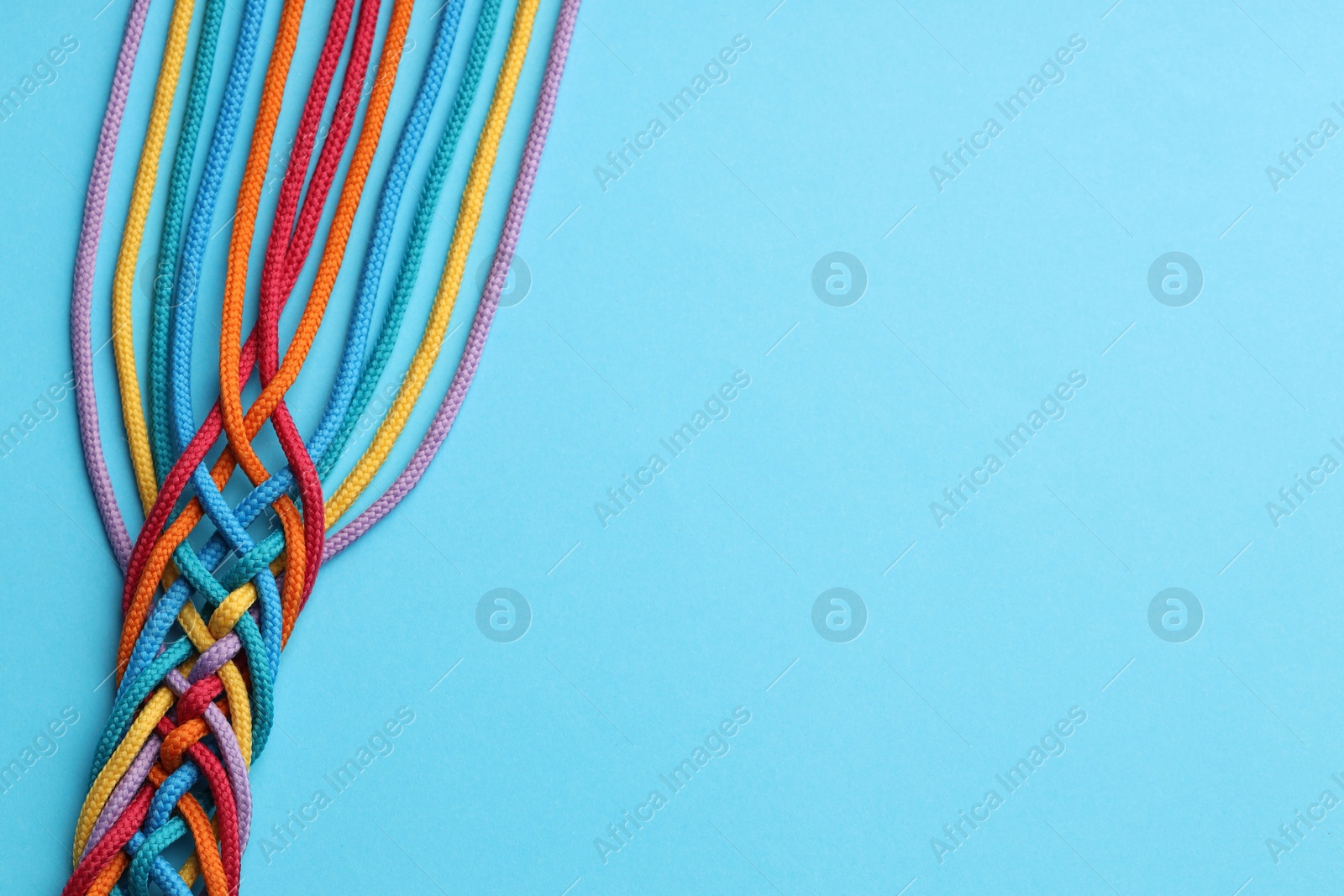 Photo of Colorful ropes tied together on light blue background, top view and space for text. Unity concept