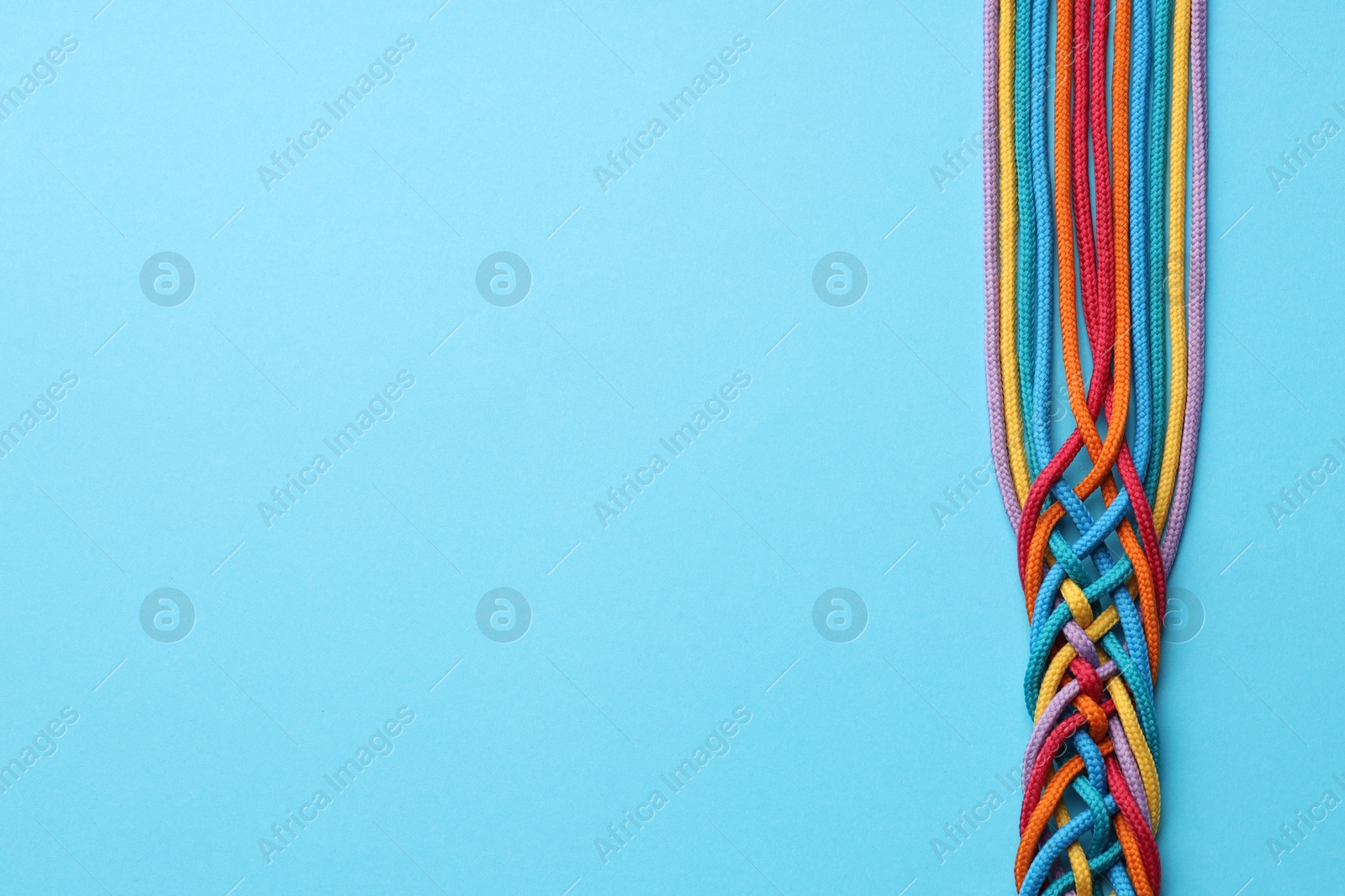 Photo of Colorful ropes tied together on light blue background, top view and space for text. Unity concept