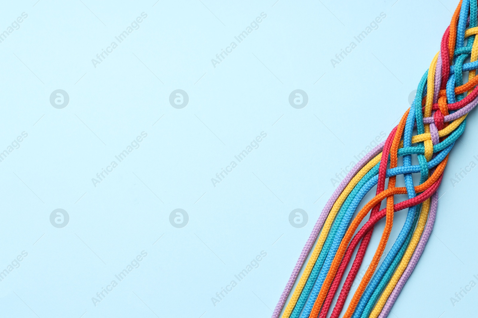 Photo of Colorful ropes tied together on light blue background, top view and space for text. Unity concept