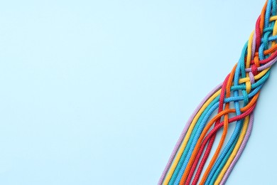 Photo of Colorful ropes tied together on light blue background, top view and space for text. Unity concept