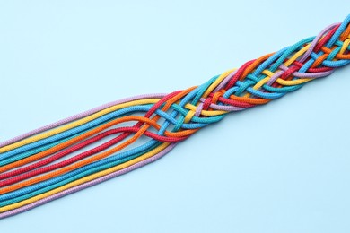 Photo of Colorful ropes tied together on light blue background, top view. Unity concept