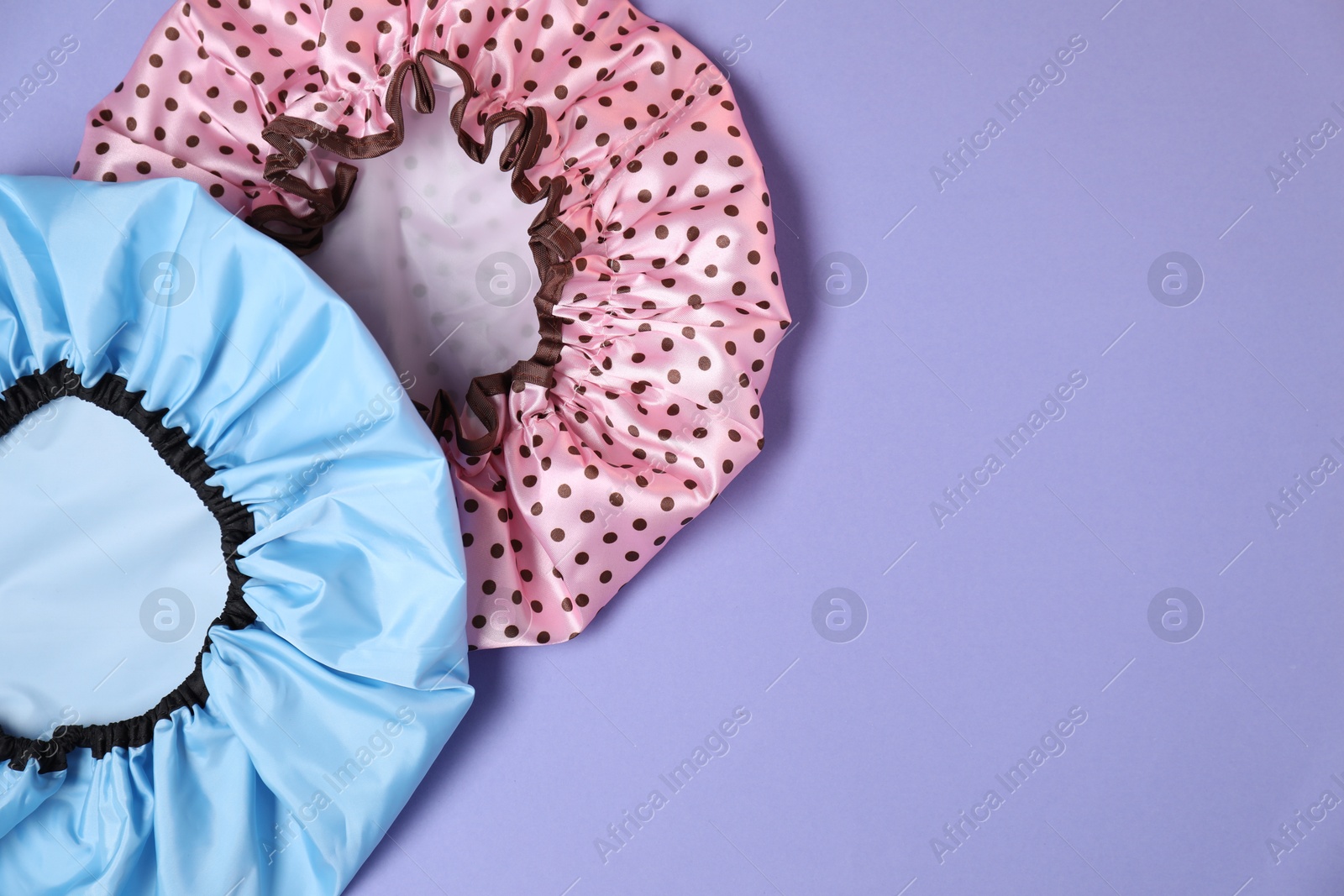 Photo of Two shower caps on lilac background, top view. Space for text