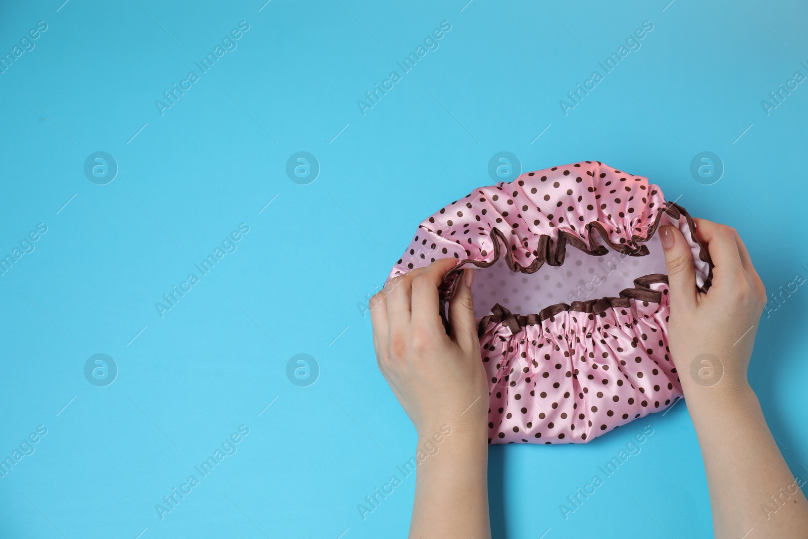 Photo of Woman with shower cap on light blue background, top view. Space for text