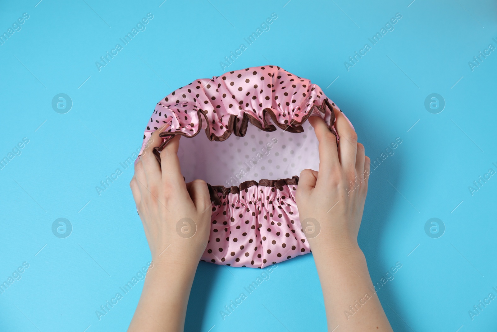 Photo of Woman with shower cap on light blue background, top view