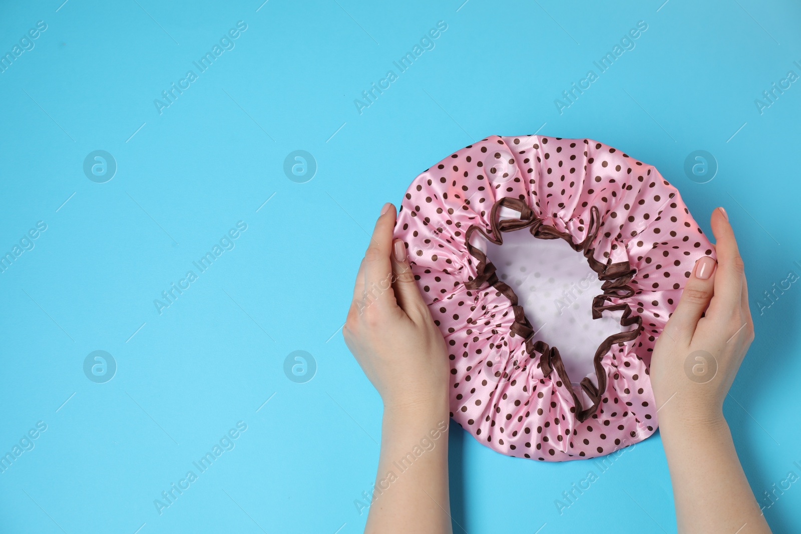 Photo of Woman with shower cap on light blue background, top view. Space for text