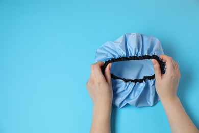 Photo of Woman with shower cap on light blue background, top view. Space for text