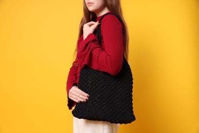 Teenage girl with handmade macrame bag on yellow background, closeup