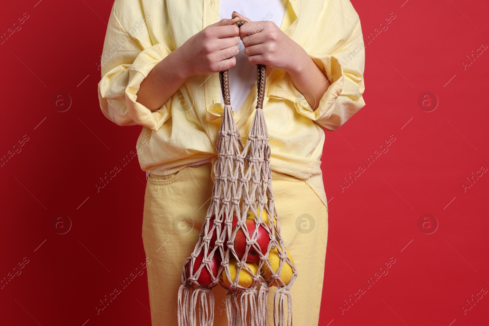 Photo of Teenage girl with handmade macrame bag on red background, closeup