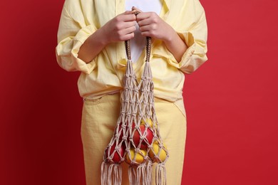 Photo of Teenage girl with handmade macrame bag on red background, closeup