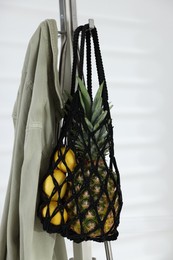 Macrame bag with fruits and jacket on clothing rack near white wall