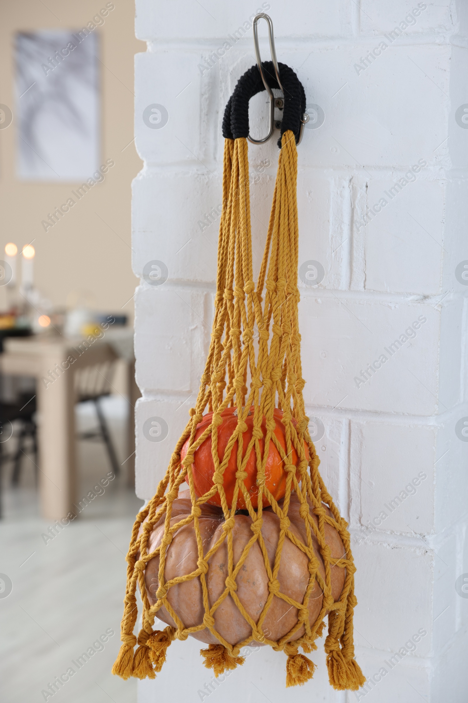 Photo of Macrame bag with products hanging on white brick wall indoors