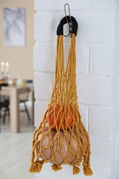 Photo of Macrame bag with products hanging on white brick wall indoors