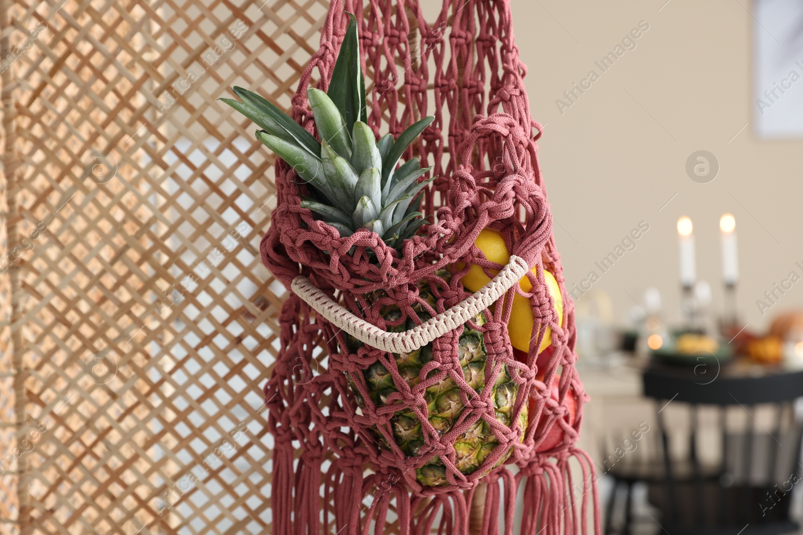 Photo of Macrame bag with fruits on folding screen indoors, closeup