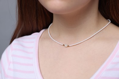 Teenage girl wearing stylish necklace on grey background, closeup